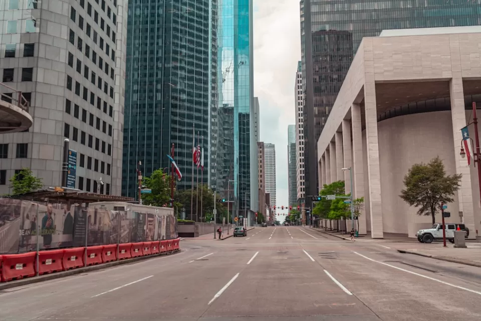 Large brutalist building and skyscrapers viewed from middle of wide street in downtown Houston, Texas.